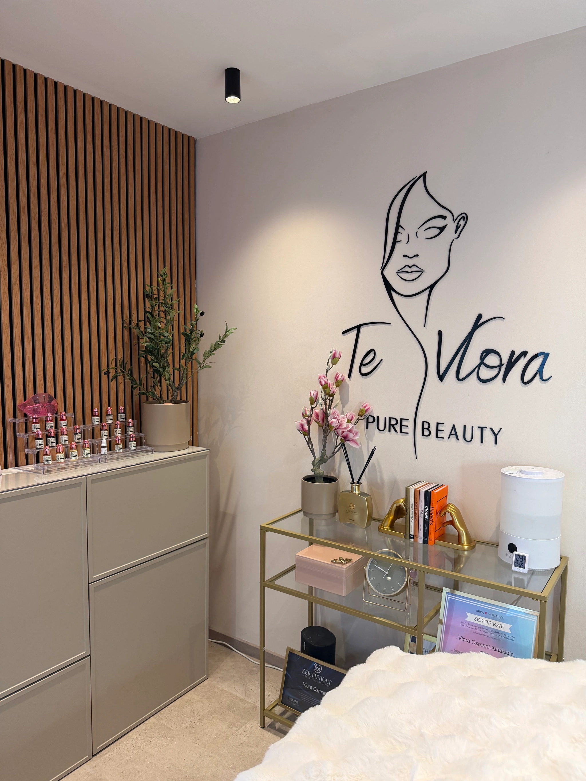 Ecke des Studios mit dem Te-Vlora-Logo an der Wand, goldenem Regal und Sideboard